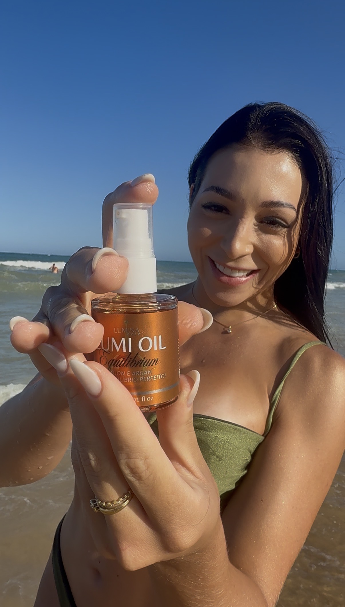 Cliente segurando Lumi Oil Equilibrium na praia